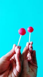 Cropped image of hand holding lollipops against blue background