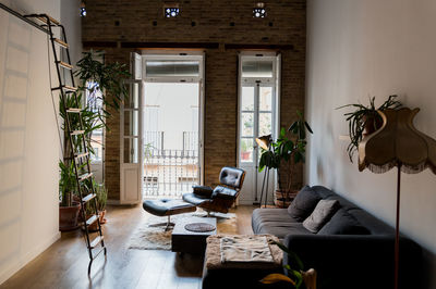 Interior of living room with green potted plants and comfortable sofa in flat in loft style