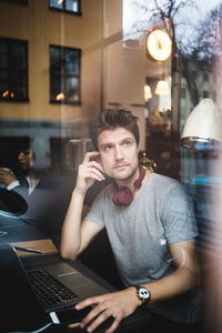 Thoughtful male entrepreneur sitting with laptop looking through window at office