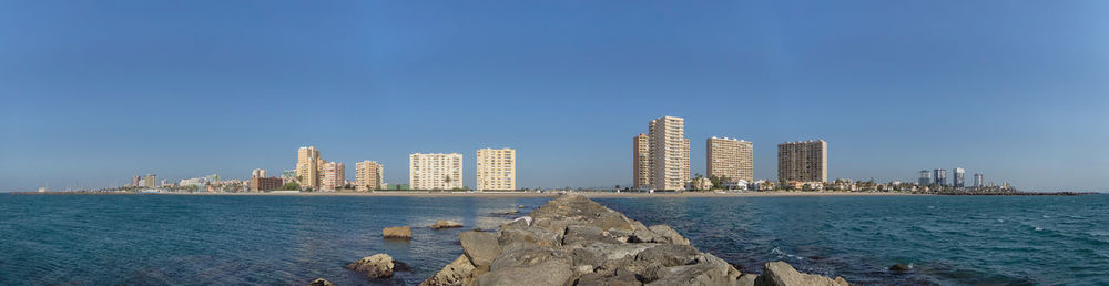 Sea by buildings against clear blue sky