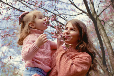 Mother and little daughter, standing in the park under a flowering cherry tree