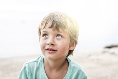 Close-up boy looking up while sitting on beach against sky