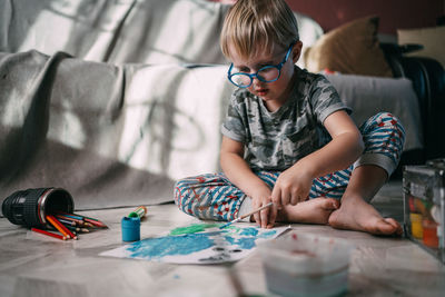 Front low angle view of child sitting on floor at home drawing