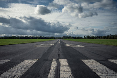 Road passing through airport runway against sky