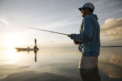 A fisherman wades while fly fishing in keys with boat in background