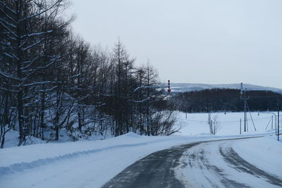 Snow covered road amidst trees against sky