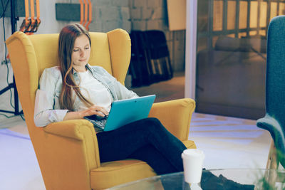 Young woman using phone while sitting on chair