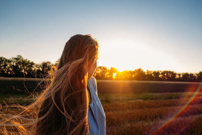 Peaceful woman with long hair in blue linen dress spending time in nature on summer day in sunset