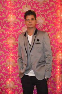 Portrait of young man standing against illuminated curtain