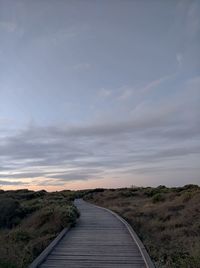 Empty road amidst field against sky