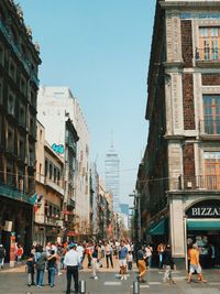 People walking on city street amidst buildings against clear sky