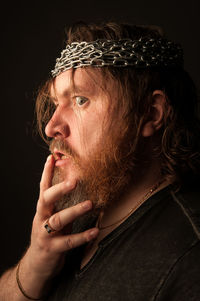 Profile view of mid adult man with beard wearing chains on head against black background