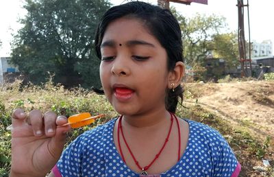 Close-up of girl eating popsicle while standing on field