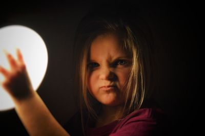 Close-up portrait of angry girl holding light against black background