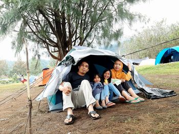 Portrait of people sitting in tent against trees