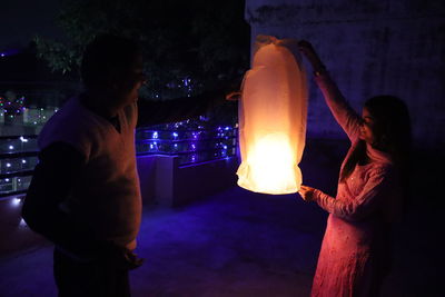 Man and woman standing against illuminated fire at night