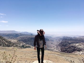 Woman wearing hat while standing on rock against blue sky