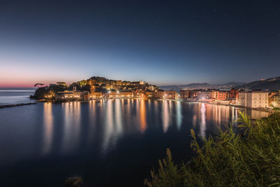 Illuminated buildings by lake against sky in city at night, bay of silence, sestri levante, italy 