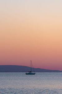 Scenic view of sea against clear sky during sunset with sailboat