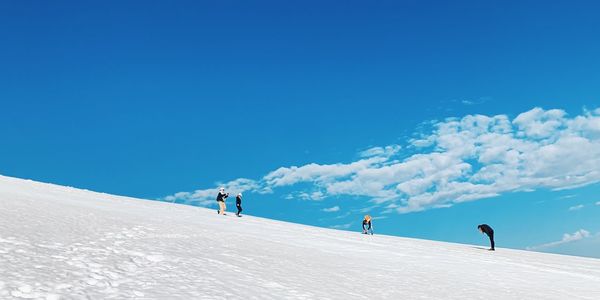 People on snowcapped mountain against blue sky