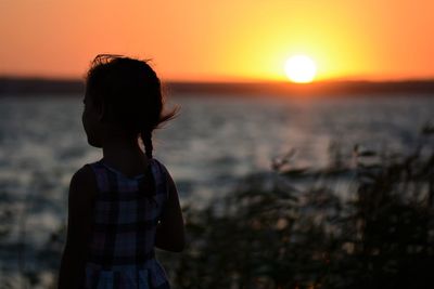 Silhouette girl standing at beach against sky during sunset