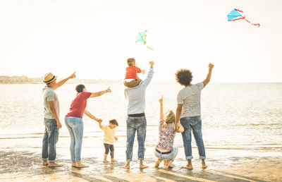 Family flying kites at sea shore against clear sky