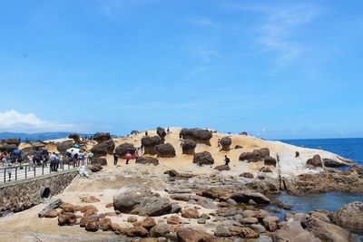 People on rocks by sea against blue sky