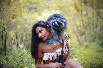 Young woman in traditional clothing carrying raccoon in forest