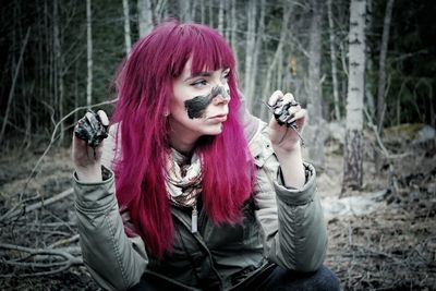 Redhead woman with mud on face crouching in forest