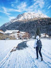 Full length rear view of person walking on snowy field against mountains during winter