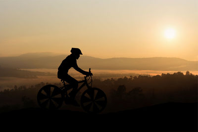 Silhouette man riding bicycle on mountain against sky during sunset