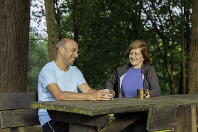 Mature couple sitting on bench and table sharing time together in natural green enviroment