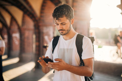 Young man using mobile phone while standing on footpath in city