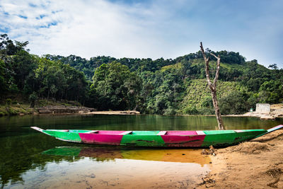 Isolated wood boat with water refection at calm river surrounded by dense green forests at morning