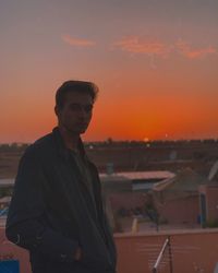 Portrait of young man standing against orange sky