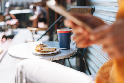 Paper cup with coffee andcheesecake on table in outdoor cafe on background of blurred young woman