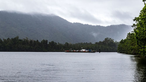 Boat sailing on river by trees against sky