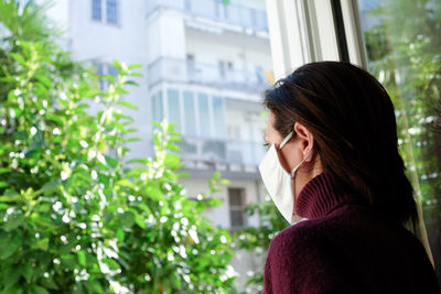 Woman wearing mask while looking through window