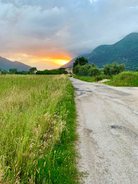 Road amidst field against sky during sunset