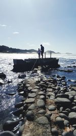 People standing on rocks in sea against sky