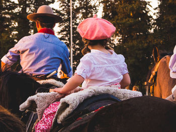 Rear view of two people riding horse on sunset