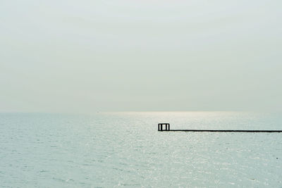 Wooden posts in sea against clear sky