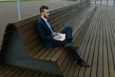 Young businessman writing in book while sitting on bench