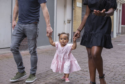 Frontal view of a family walking their young daughter