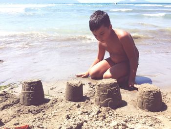 Shirtless boy making sandcastle at beach