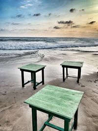 Empty chairs and table on beach against sky