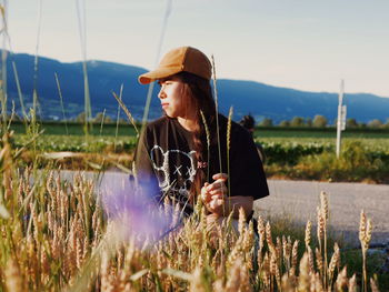 Woman sitting by plant against sky