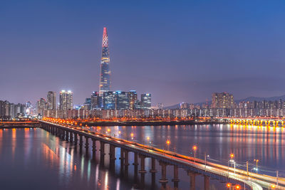 Illuminated buildings by river against sky at night