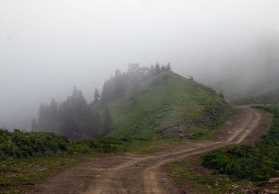 Dirt road amidst green landscape against sky