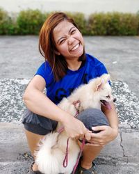 Portrait of smiling woman with puppy sitting on sidewalk